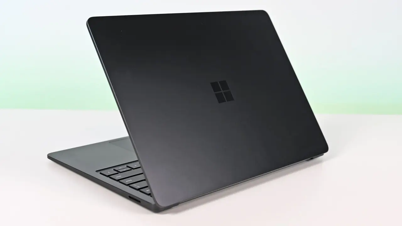 Surface Laptop for Business 8th Edition with a closed screen featuring a Windows logo, resting on a white surface. The background is a soft gradient from light blue to green.