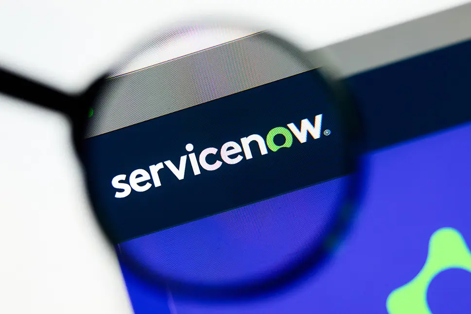 Closeup of ServiceNow website page on a laptop screen. Focus on ServiceNow logo under a magnifying glass.