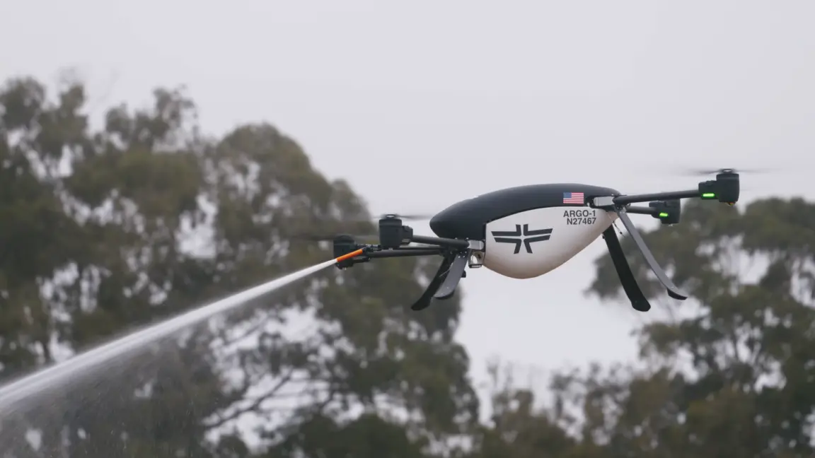 An Argo-1 quadcopter drone developed by Seneca is shown hovering in a side profile while spraying fire suppressant from nozzles at the front.