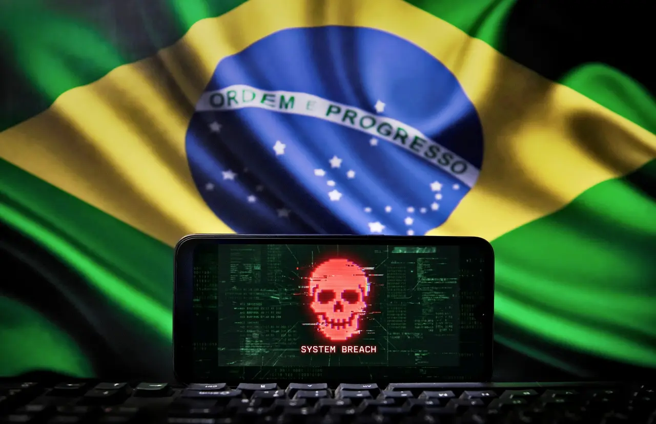 Ao fundo, bandeira do Brasil; à frente smartphone com uma caveira vermelha na tela